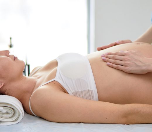Chinese Pregnant Woman Receiving Stomach Massage From Female Masseur In Spa Cabinet