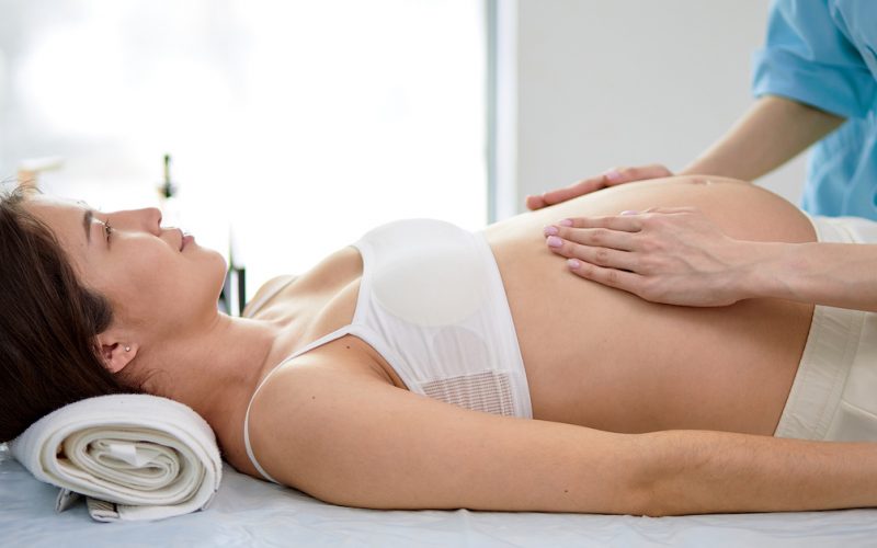 Chinese Pregnant Woman Receiving Stomach Massage From Female Masseur In Spa Cabinet