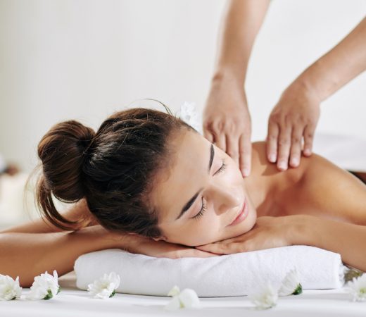Pretty young woman relaxing on bed in spa salon and getting back massage