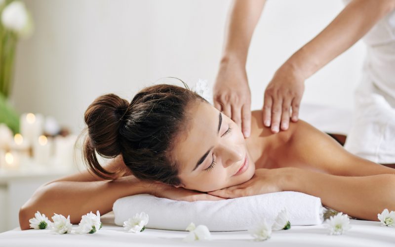 Pretty young woman relaxing on bed in spa salon and getting back massage